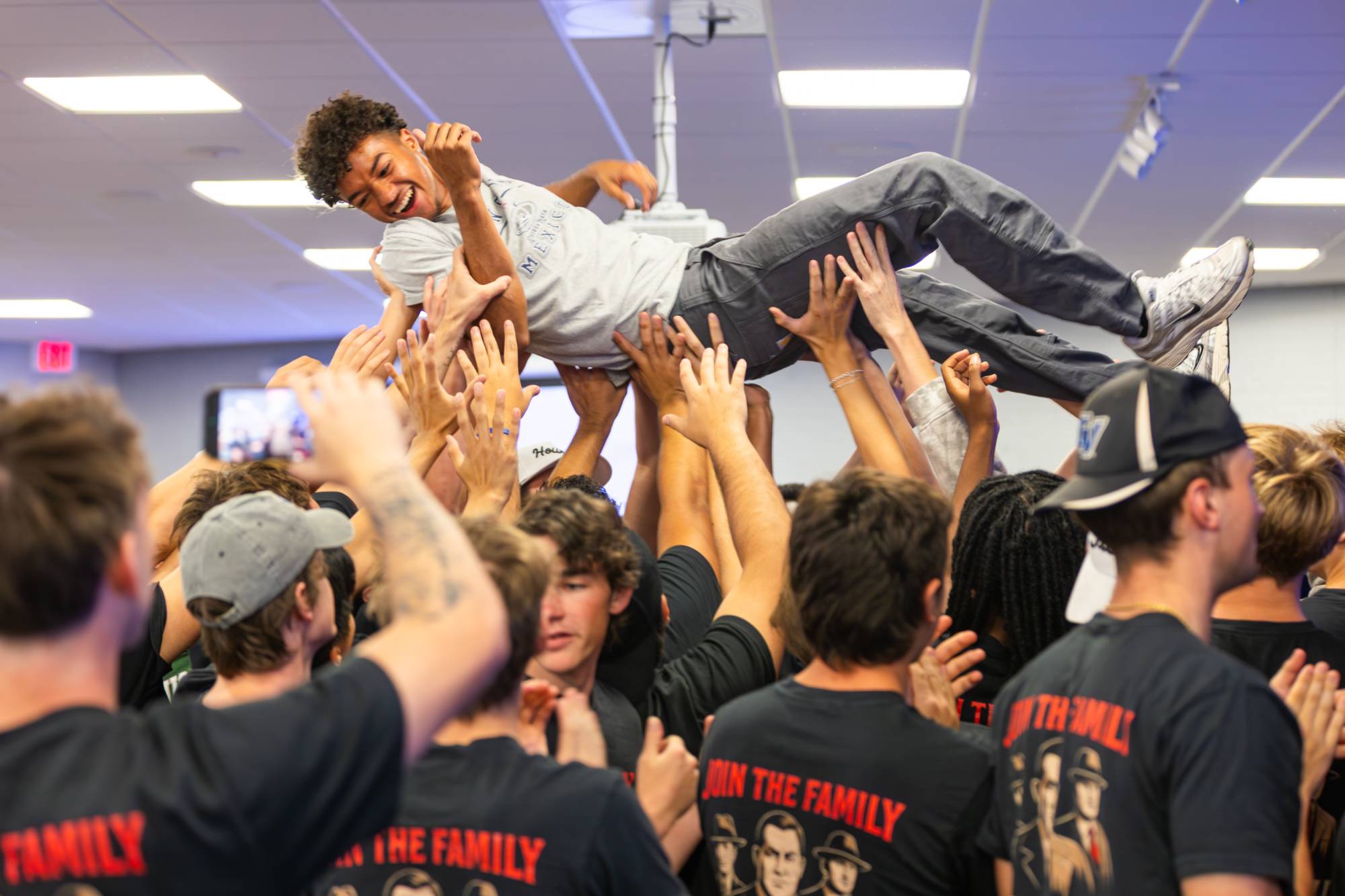 Boy being crowd surfed by crowd of fraternity brothers.